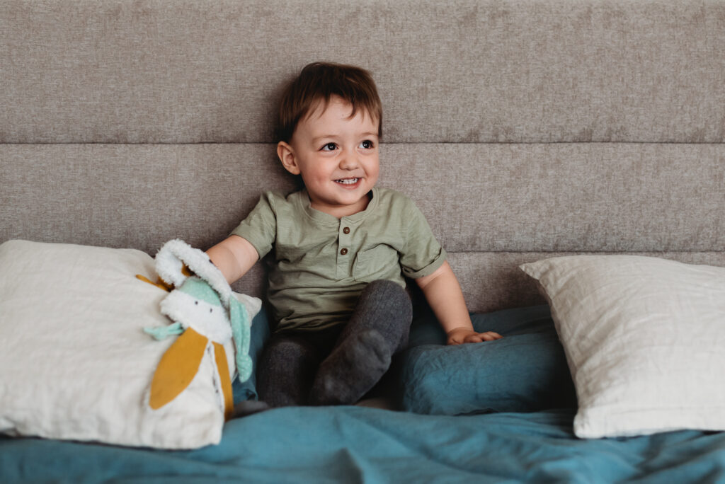 usmívající se chlapec sedící na posteli s usínáčkem