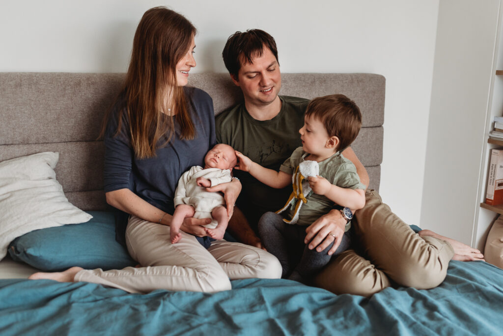rodina sedící na posteli s novorozeným synem a starším synem