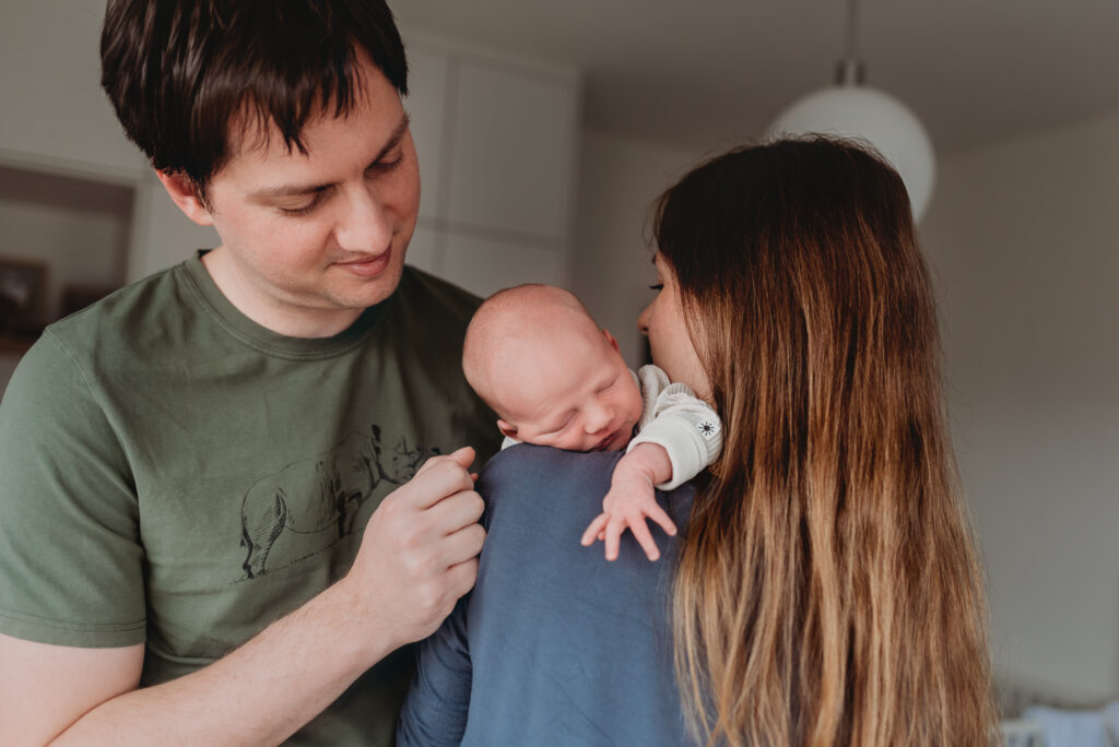 tatínek hledí na svého syna, který leží přes maminčino rameno