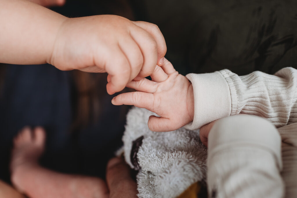 detail ruky staršího bráchy držícího novorozeného