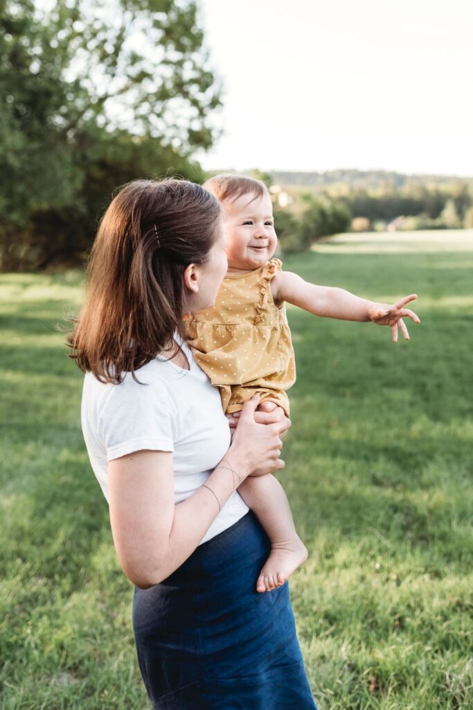 Máma drží svou dceru v náruči a ta jí ukazuje do dáli.