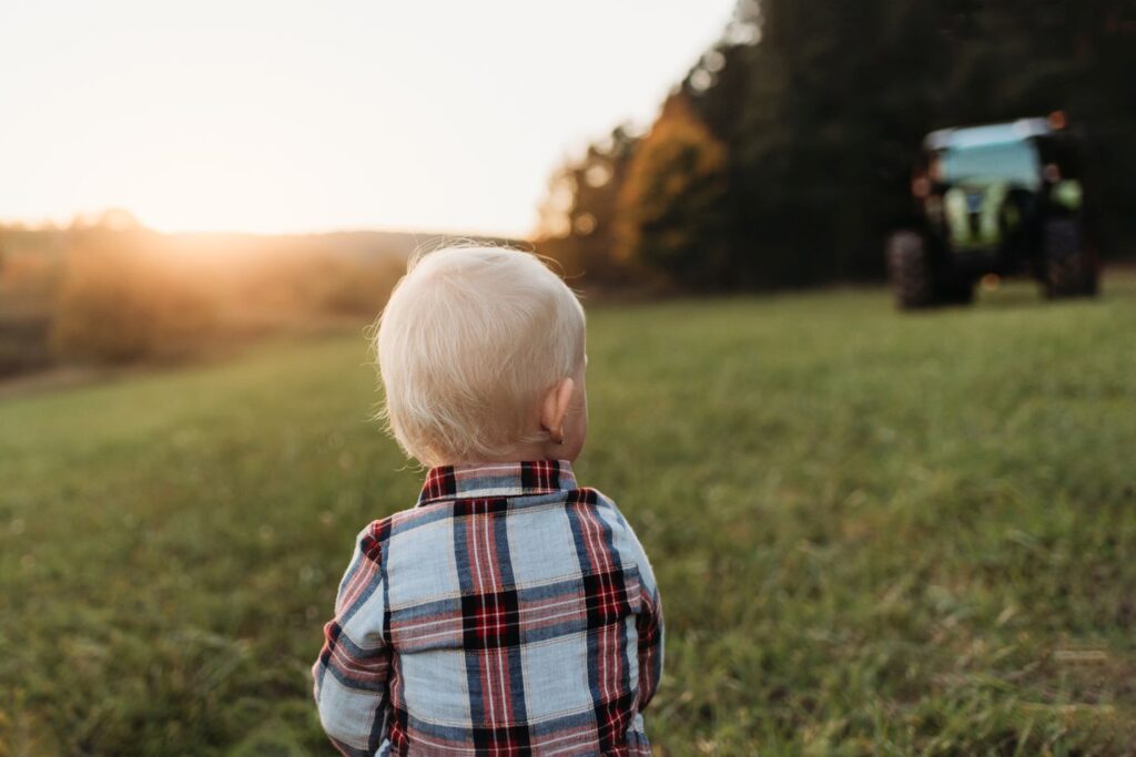 Holčička se ohlíží po traktoru na louce.