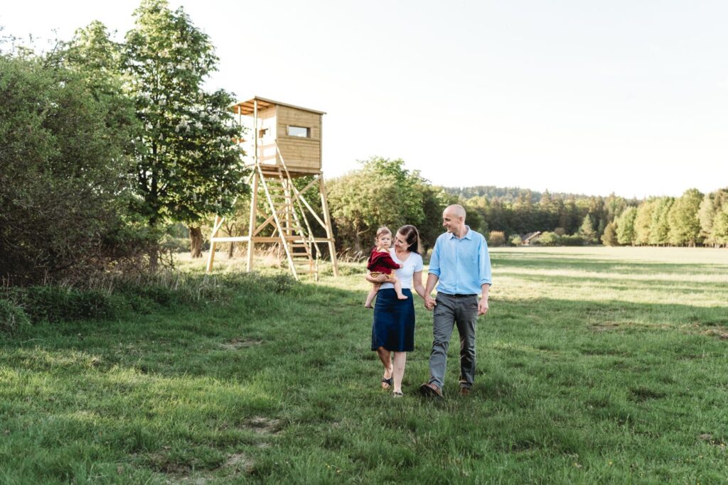 Rodiče jdou se svou malou dcerou v náruči po louce vedle posedu.