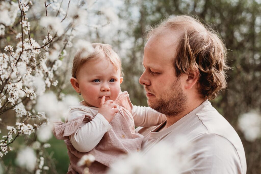 Táta drží svou dceru mezi rozkvetlými jarními květy.