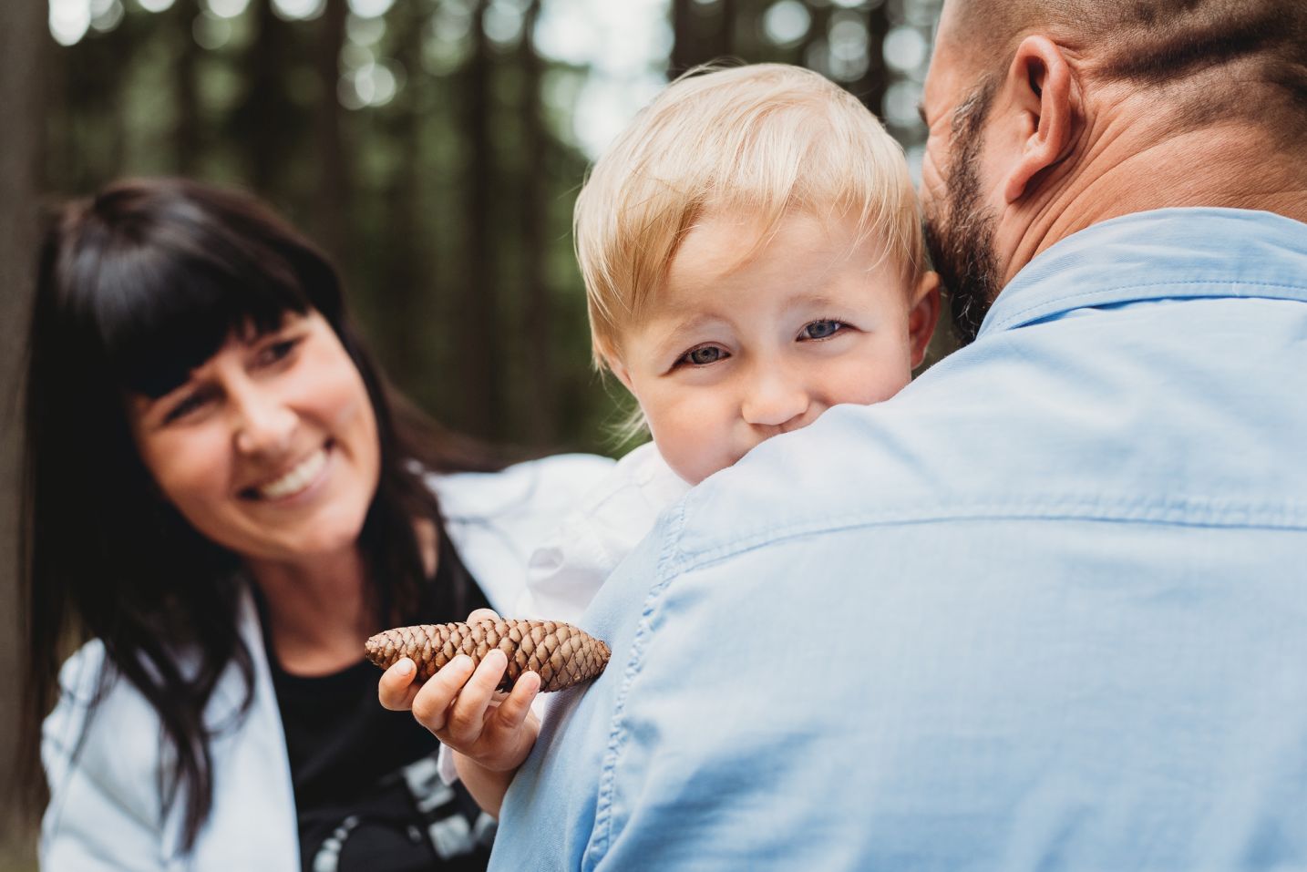 Chlapeček drží šišku a kouká přes rameno svého otce.