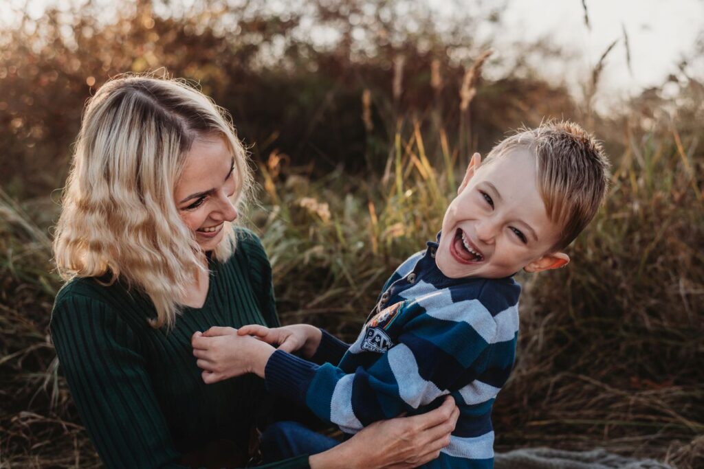 Maminka sedí na dece se synem a lochtá ho.