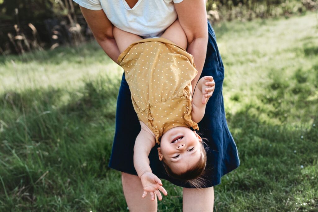 Holčička visí z maminčiny náruče hlavou dolů a mává.