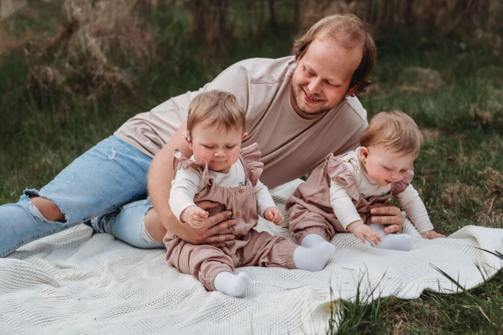 Táta sedí na dece se svými dcerami dvojčaty.