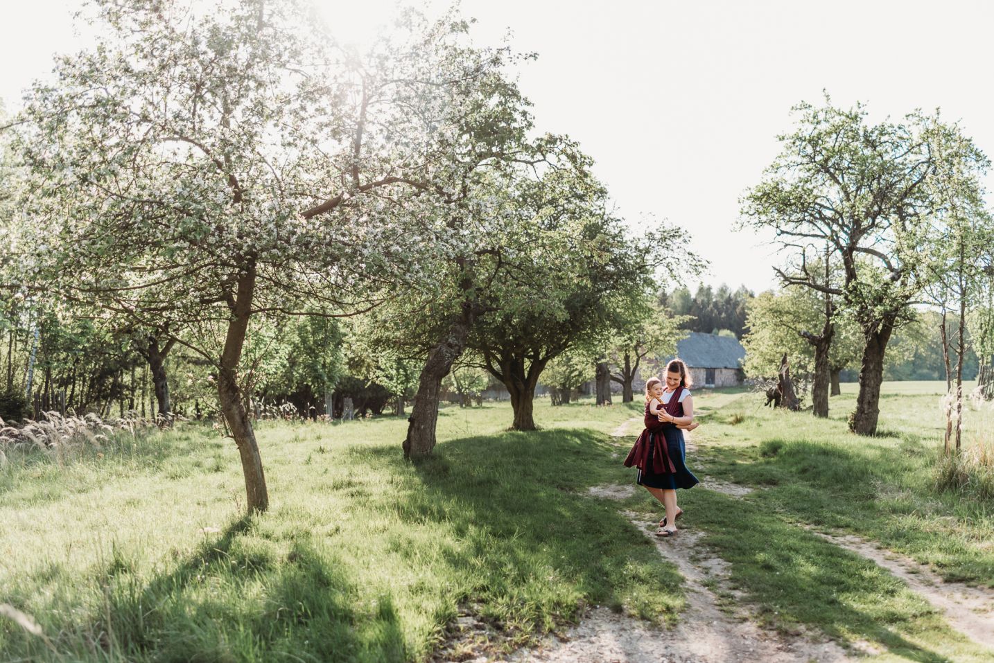 Maminka s dcerou v šátku tančí mezi rozkvetlými jarními stromy.