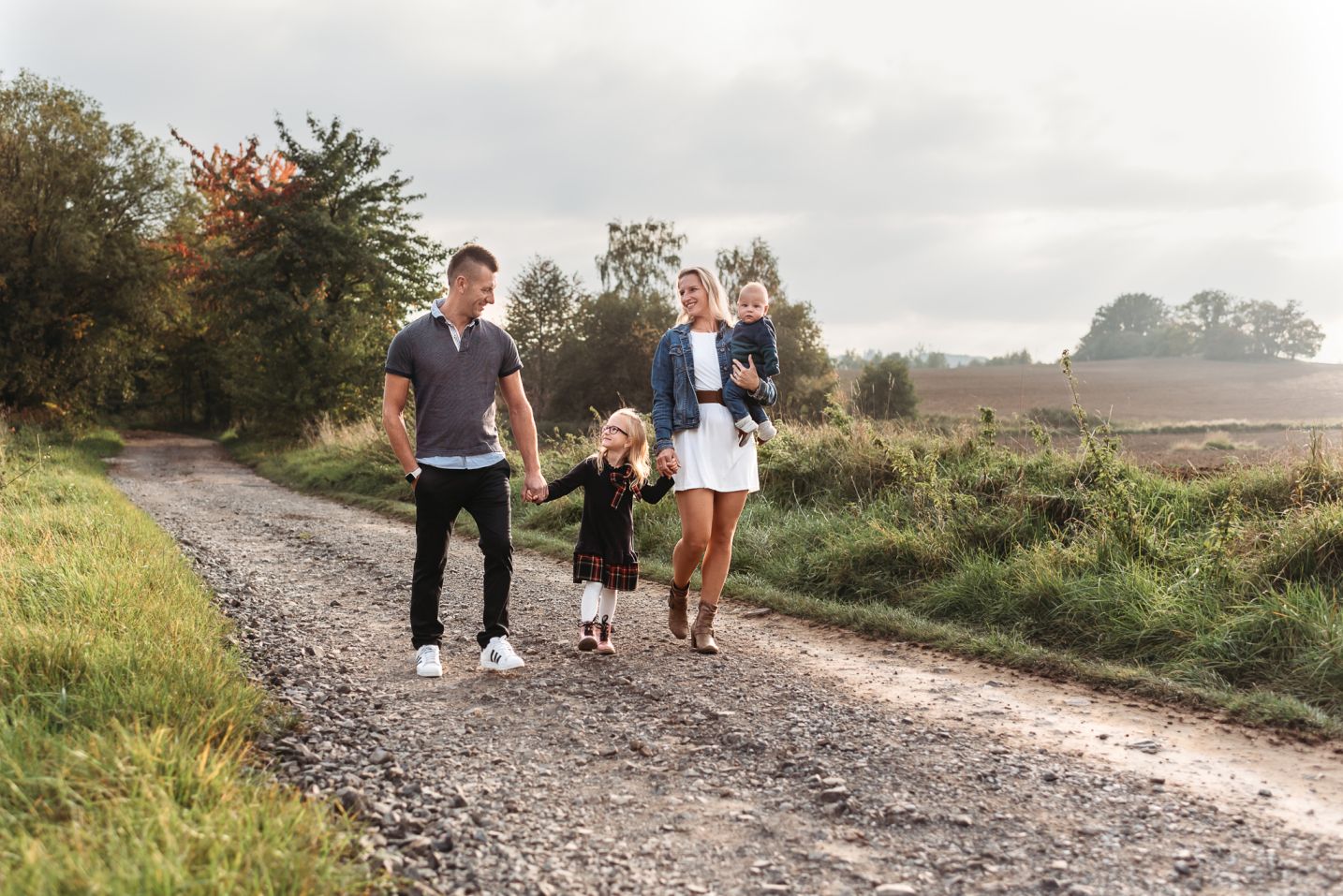 Rodina spolu kráčí na podzim při západu slunce po cestě.