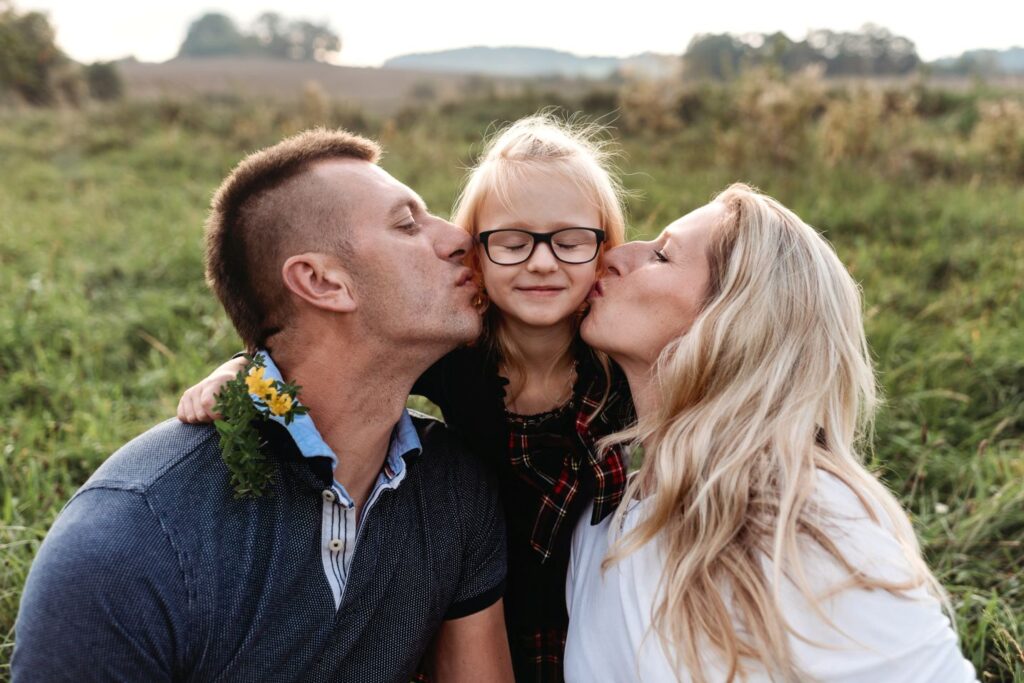 Otec a matka dávají pusu z každé strany své dceři.