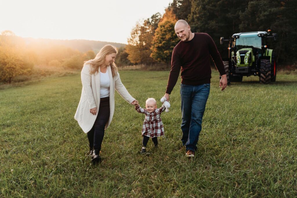 Maminka a tatínek mezi sebou drží dceru a kráčejí po louce,