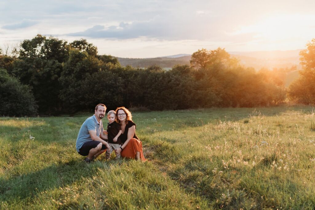 Rodina sedí na louce při západu slunce.