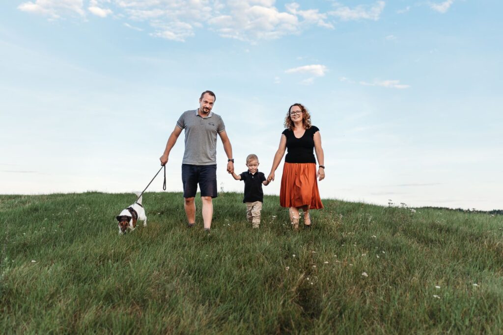 Rodina se synem a psem kráčí po louce.