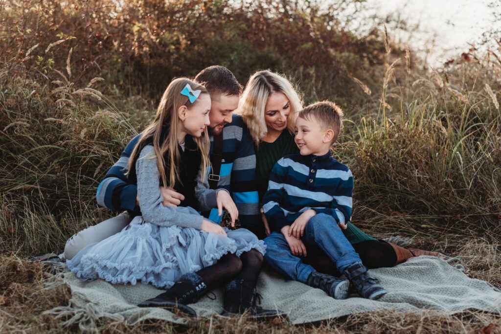 Rodina sedí na louce v suché trávě a hraje tichou poštu.