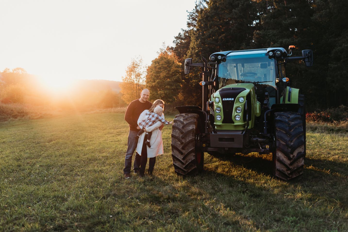 Rodina s dcerou zkoumají svůj traktor na louce při západu slunce.