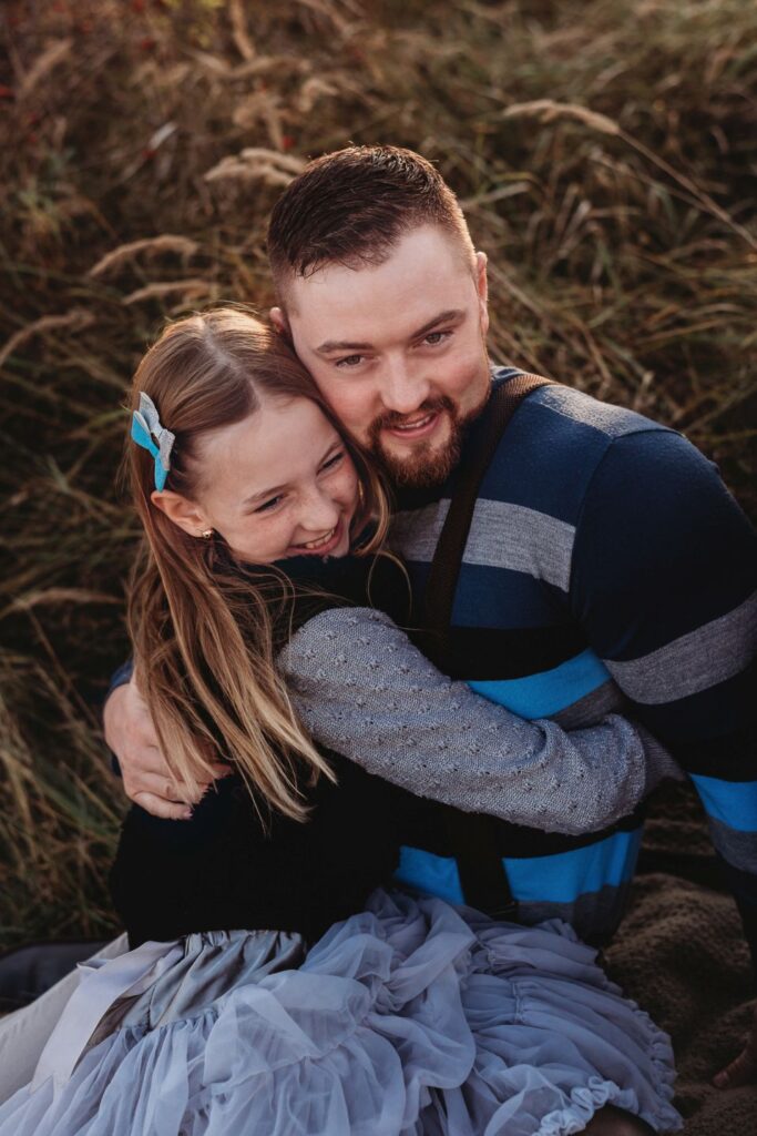 Dcera s úsměvem objímá v sedě svého tátu.