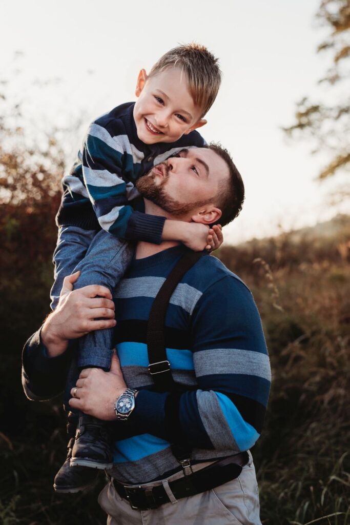 Táta drží syna na svém rameni a snaží s emu dát pusu.